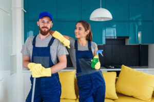 Smiling handsome man and attractive young woman as a professional cleaners stay together in the contemporary cuisine with detergents.